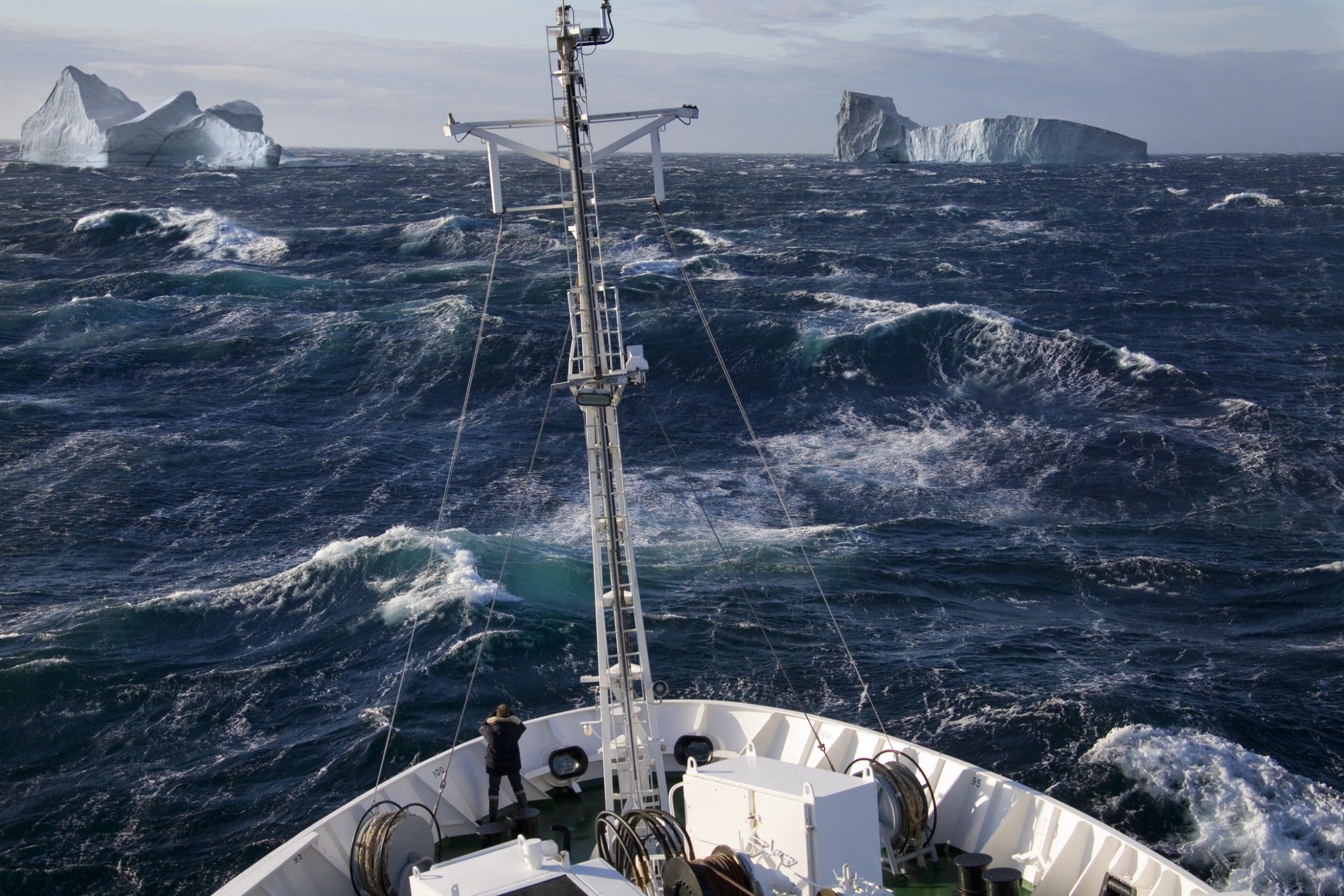 High vantage point image of man standing on the bow of a lage ocean going vessel against a background of rough seas