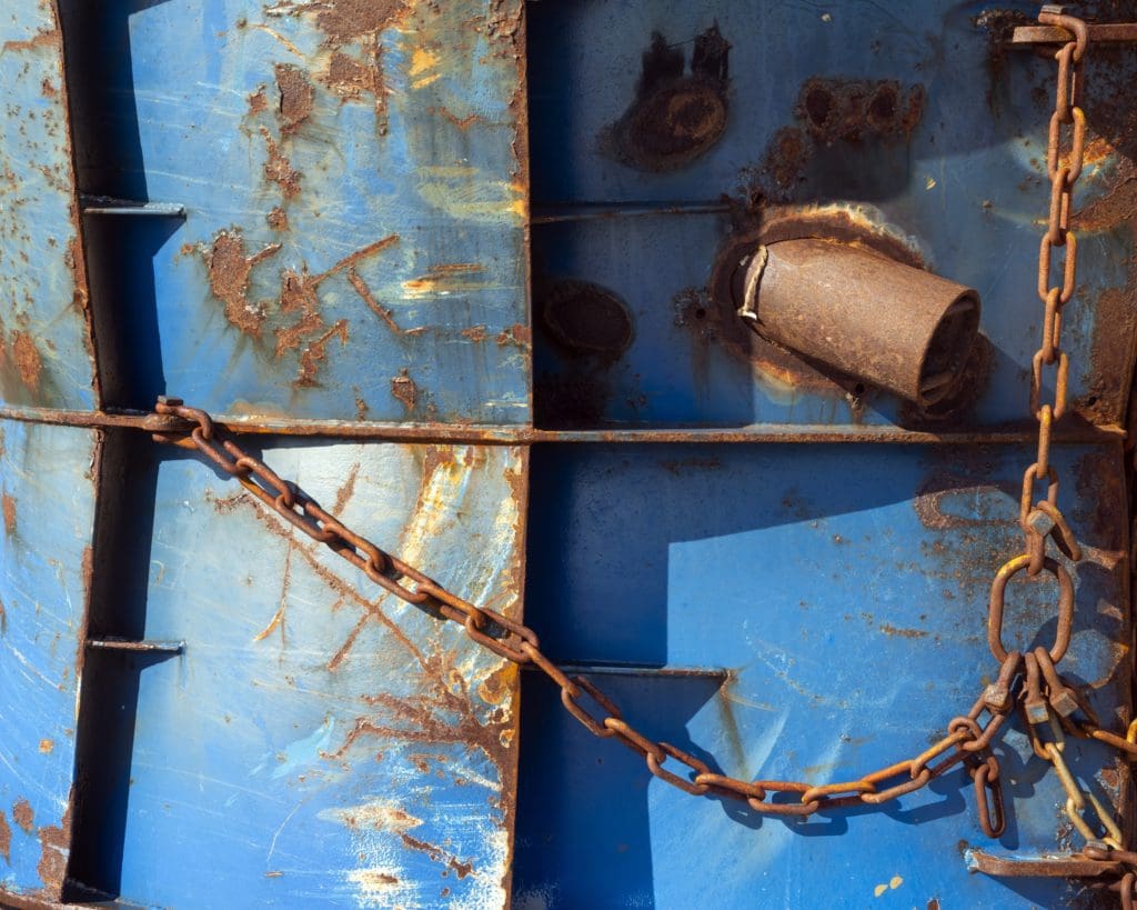 close up view of blue ship hull w/ rusted patches and chain