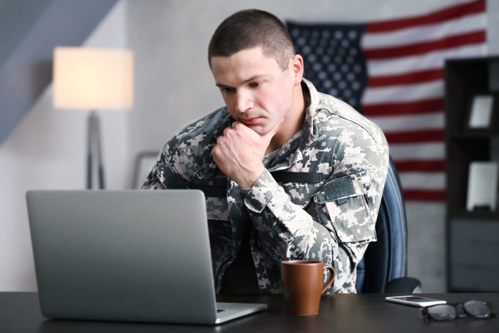 Soldier sitting at desk leaning on one elbow studying a laptop screen