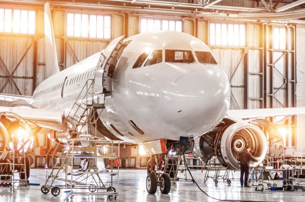 Passenger commercial airplane on maintenance of engine turbo jet and fuselage repair in airport hangar. Aircraft with open hood on the nose and engines, as well as the luggage compartment