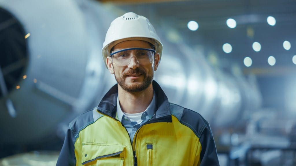 Portrait of Smiling Professional Heavy Industry Engineer / Worker Wearing Safety Uniform, Goggles and Hard Hat.