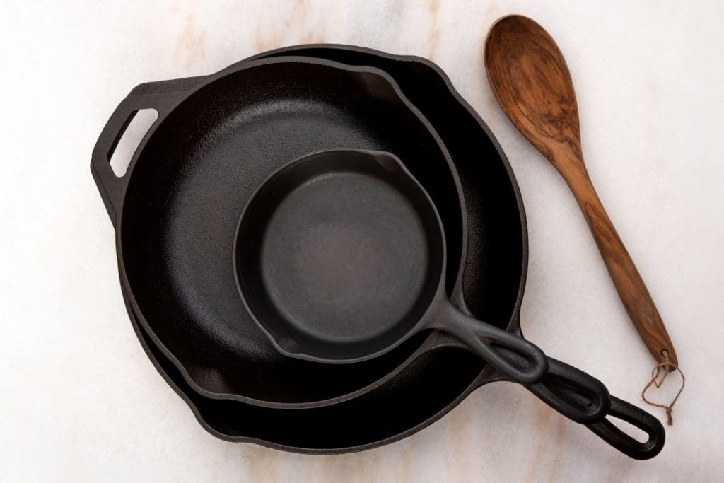 multiple sized cast iron pans stacked on one another with a wooden spoon next to them