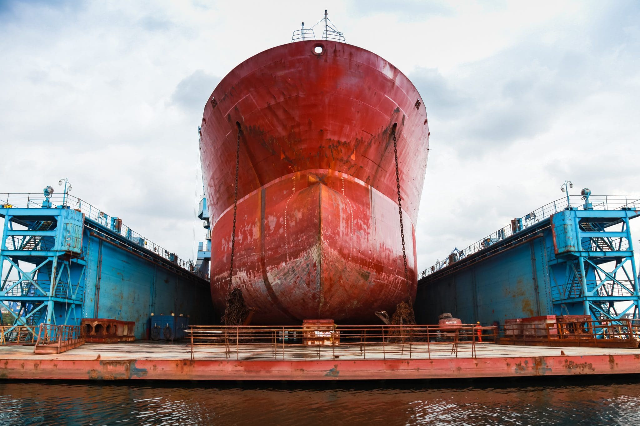 A large red tanker ship docked for repair at a shipyard.