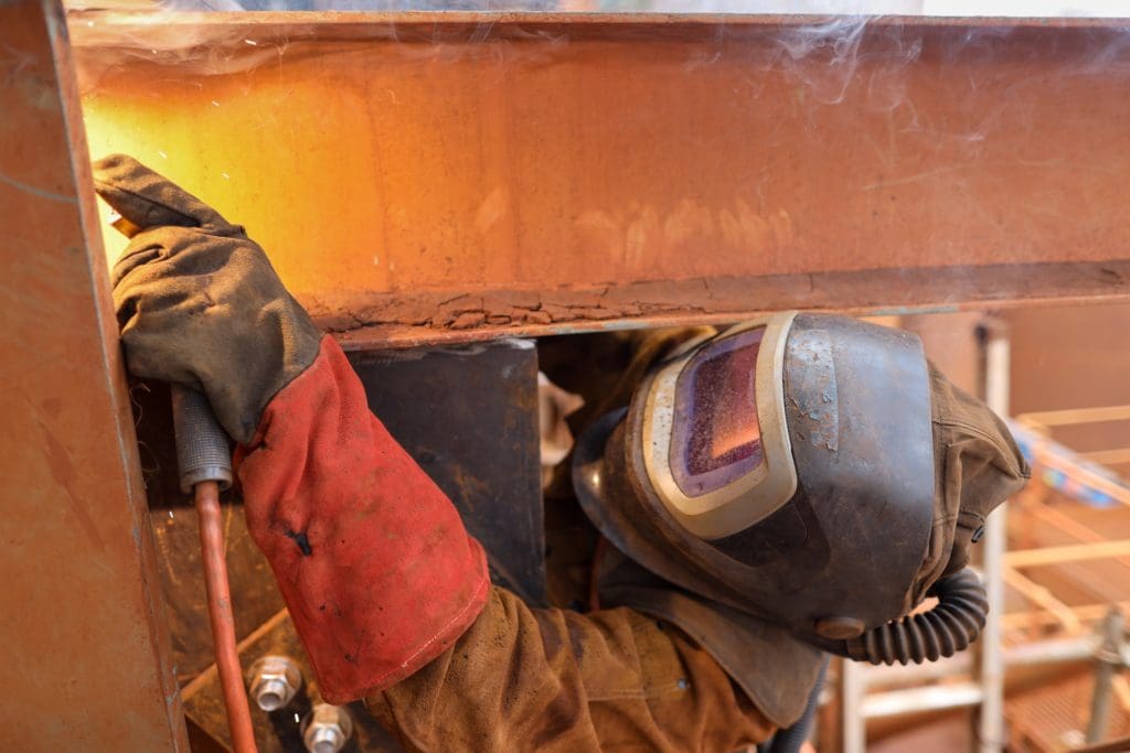 Macro pic of maintenance welder wearing red safety glove welding helmet with power air purifying respirator while performing welding a difficult task condition to protect from the toxic fume