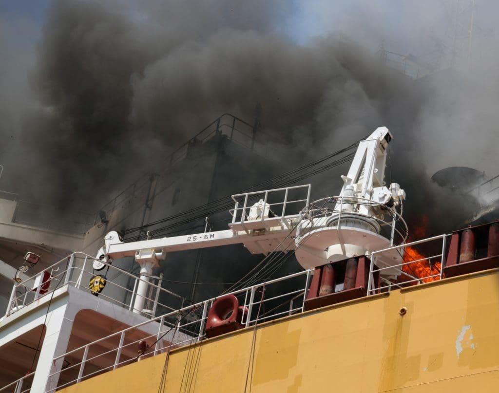 Smoke hovering over a large yellow ship during a shipyard fire. Mobile cold spray repair can help reduce risk of shipyard fires.