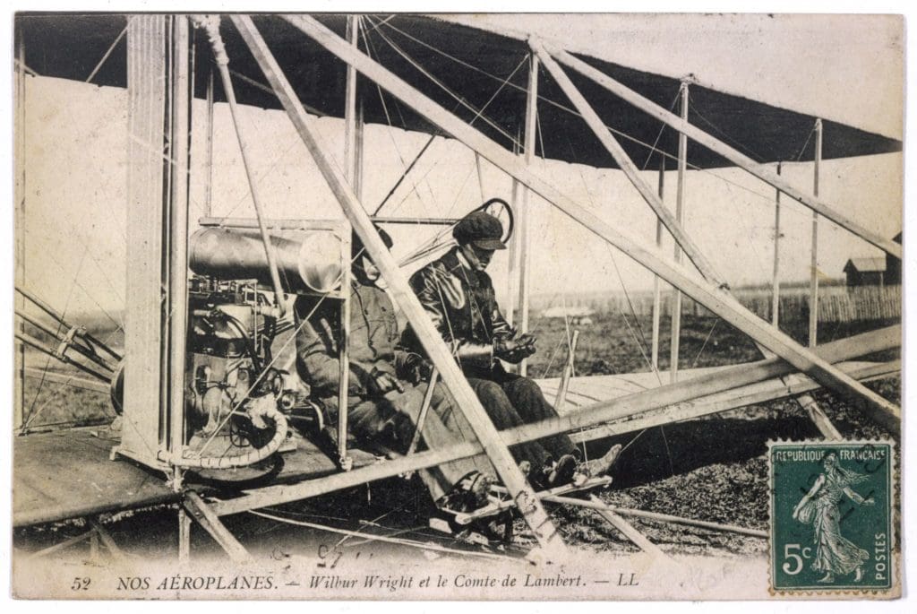 sepia photo of 2 men seated in Wilbur Wright plane dated 1909