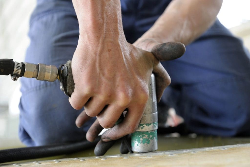 worker's hands holding a drill making holes on a plane body preparing it for aircraft sheet metal construction and repair