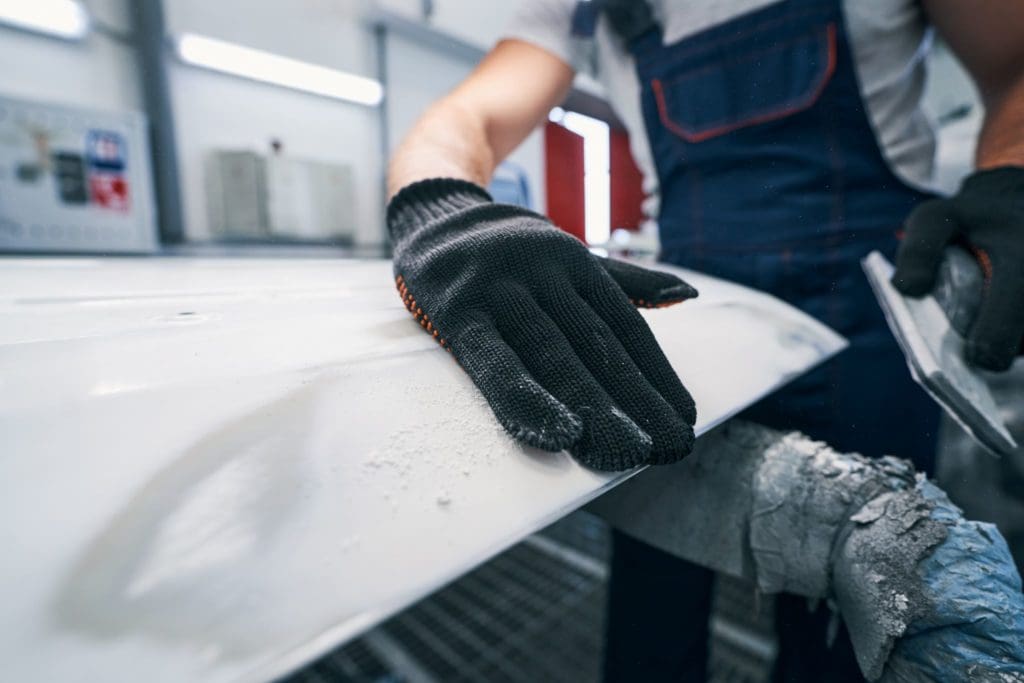 Technician wiping powder off a metal panel with a black gloved hand