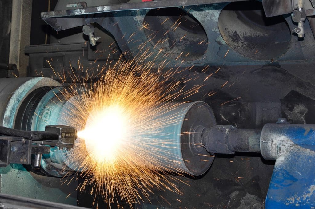thermal coating gun sprays sparks as it targets metal surface for repair to create a corrosion resistance coating