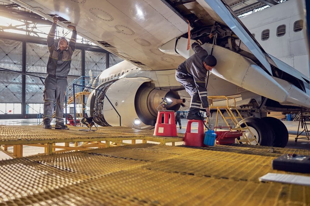 Full length portrait of two engineer workers in uniform fixing and checking commercial airplane in hangar