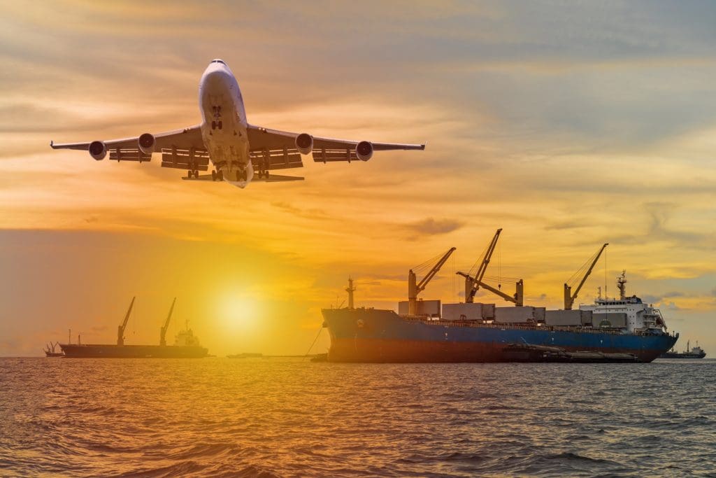 Commercial passenger airplane fly over a large general cargo ship sailing in the sea near the coast and spread the wheel prepare landing to airport in evening while golden sunset