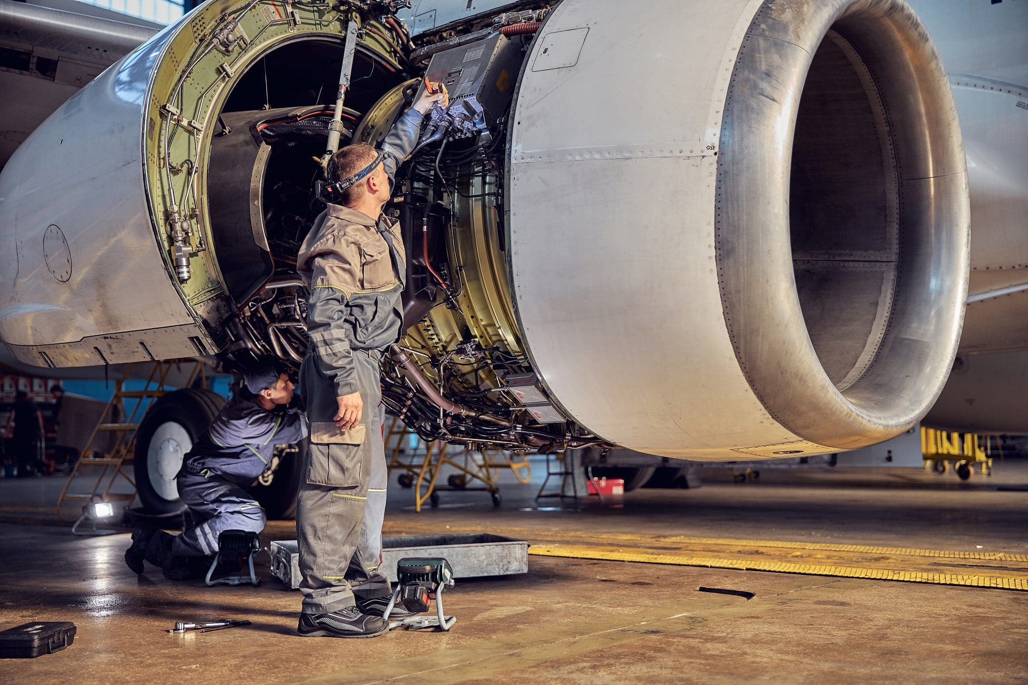 Full length portrait of 2 technicians who are repairing aircraft in the aviation hangar