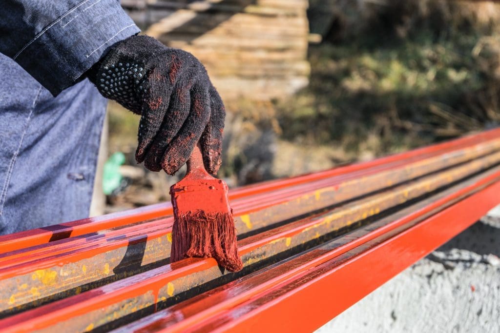 House painter paints metal structures. Protective coating of steel closed profiles with primer iron oxide red. Paint is acting as a corrosion resistant coating
